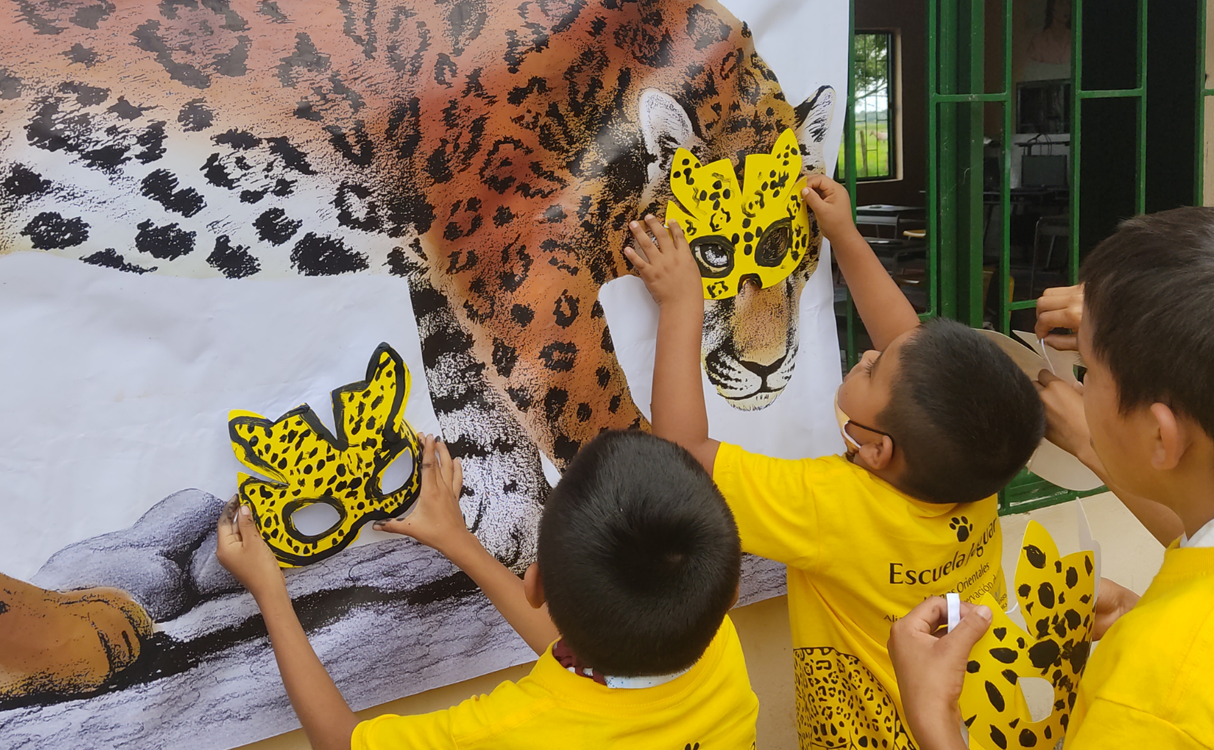 Students adding jaguar masks that they've created to a poster