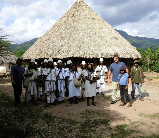 Group of people standing outside of a building with a thatched roof 